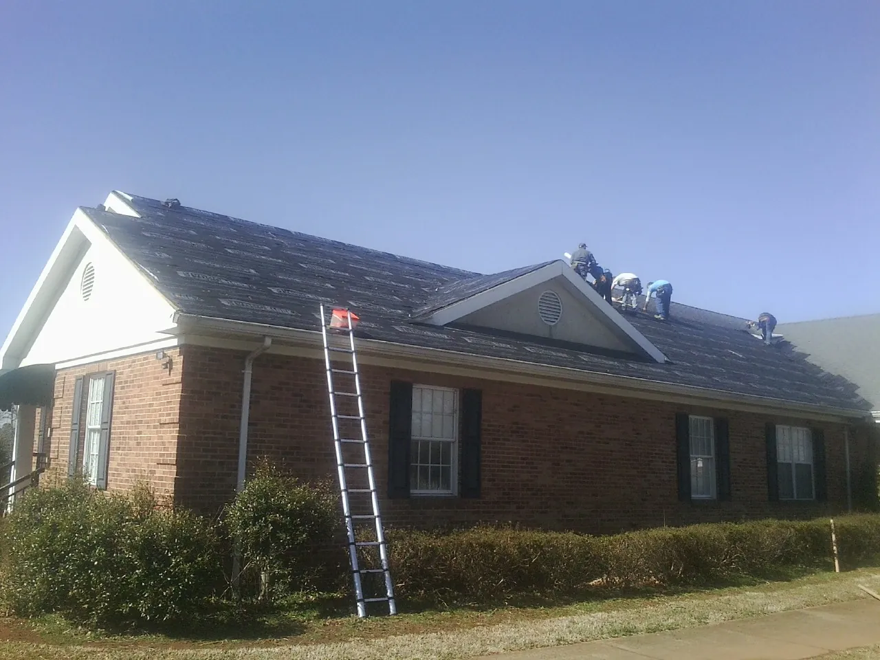Crew tearing shingles off a brick ranch roof with a ladder set — Metal Roof Repair work by our crew in Greenville