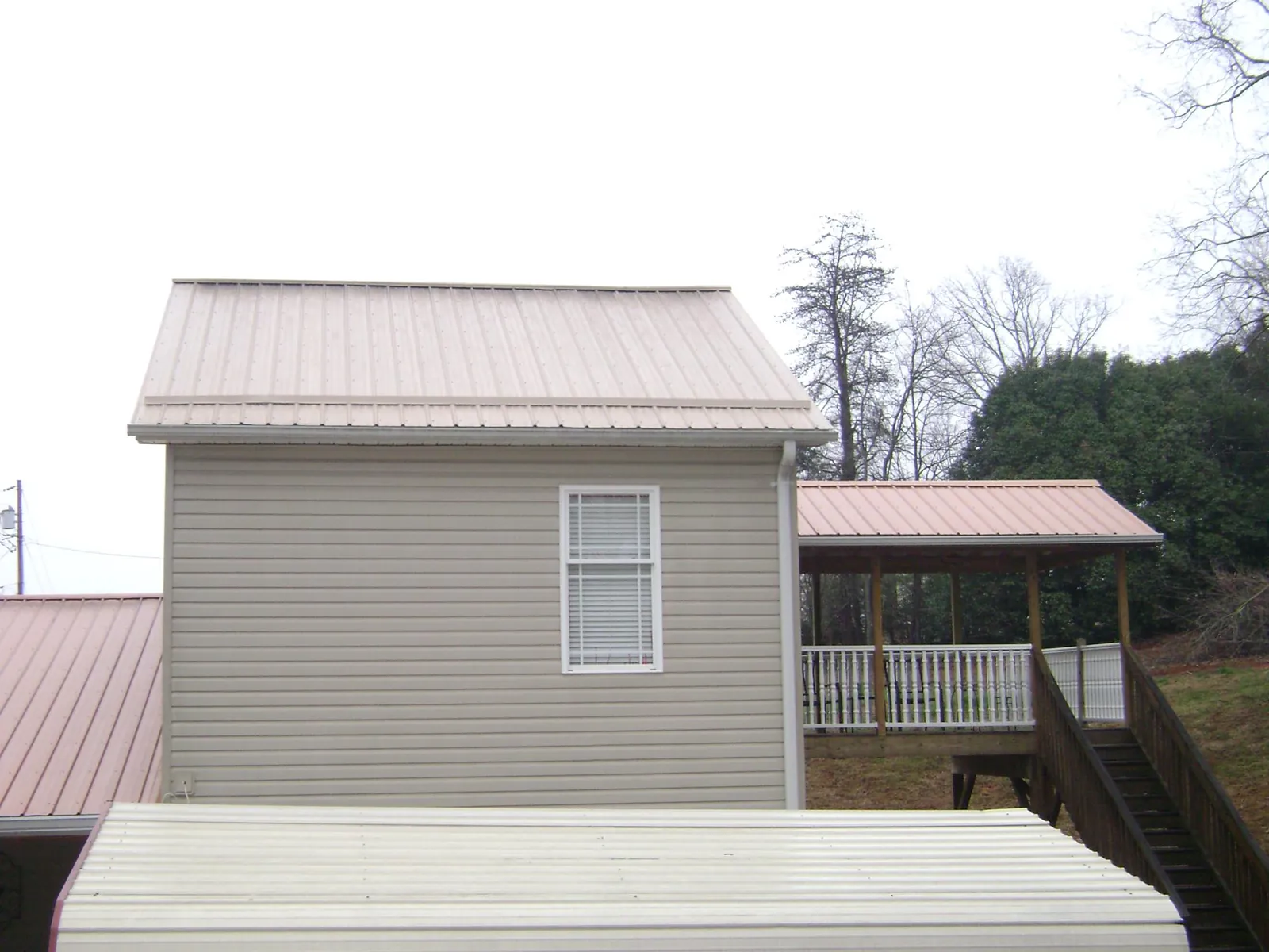 Tan metal roofs on a two story addition and attached porch, from a Roof Replacement job in Greenville